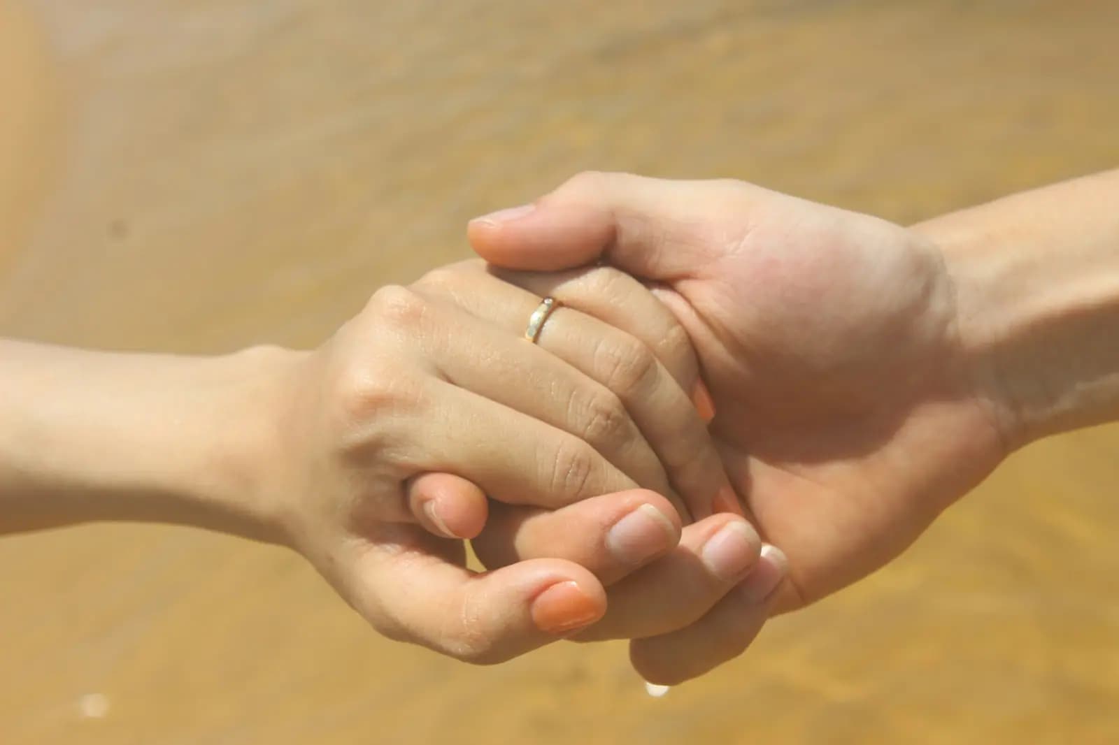 Close-up of two people holding hands against a soft golden background
