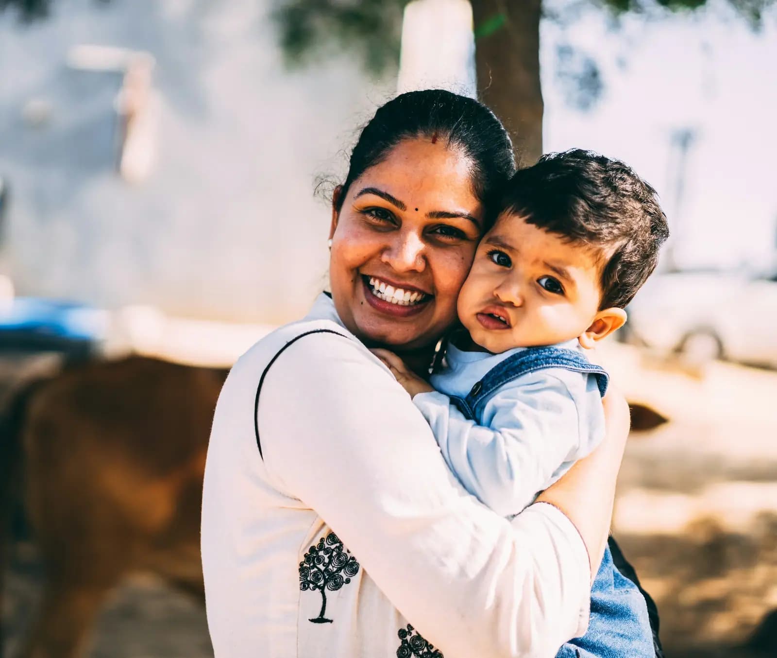 A smiling mother hugs her young son tightly, his cheek pressed against hers