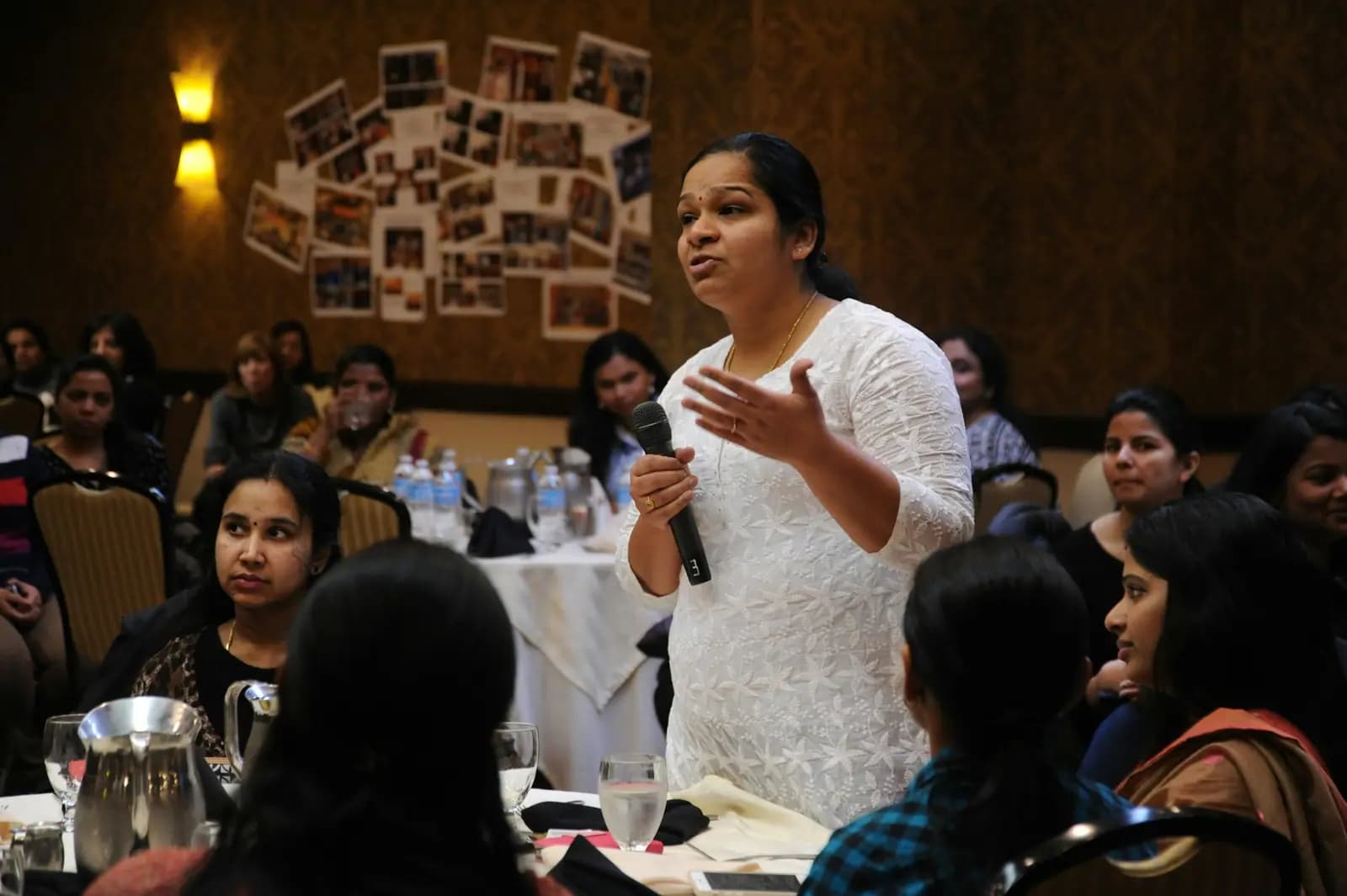 A woman with a microphone speaks to a room of seated participants at a workshop