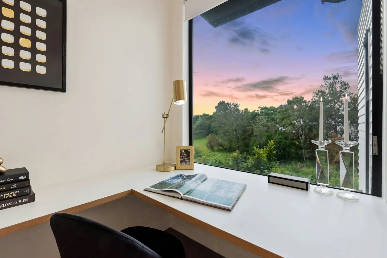 A quiet corner desk beside a large window, with a lamp, books and an open magazine in evening light