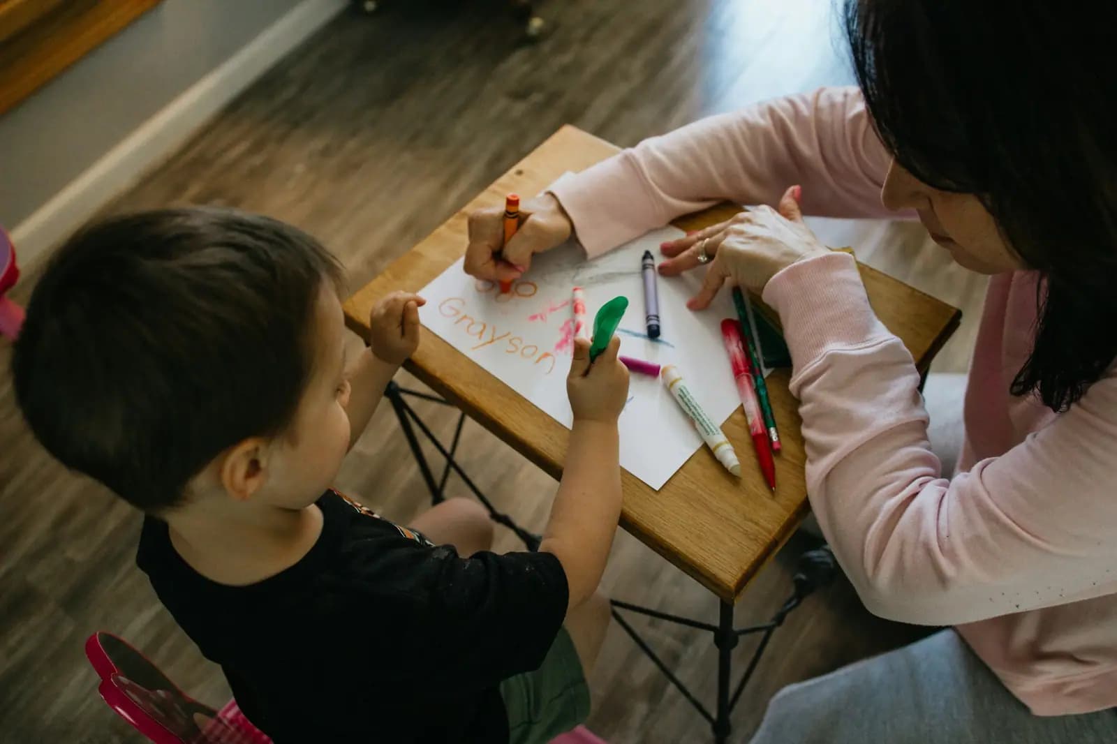 An adult and a young child colour a drawing together at a small table at home